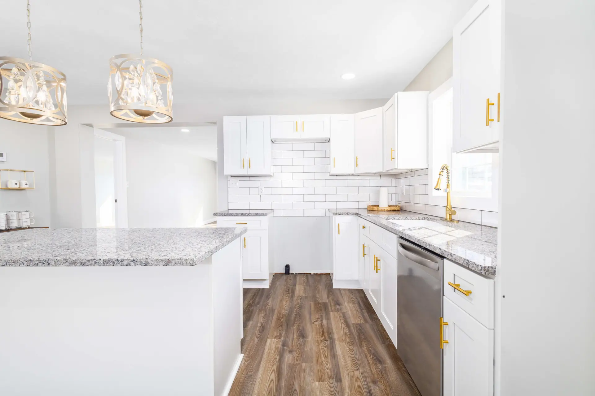 Renovated kitchen with white cabinets, granite counters, and gold pendants