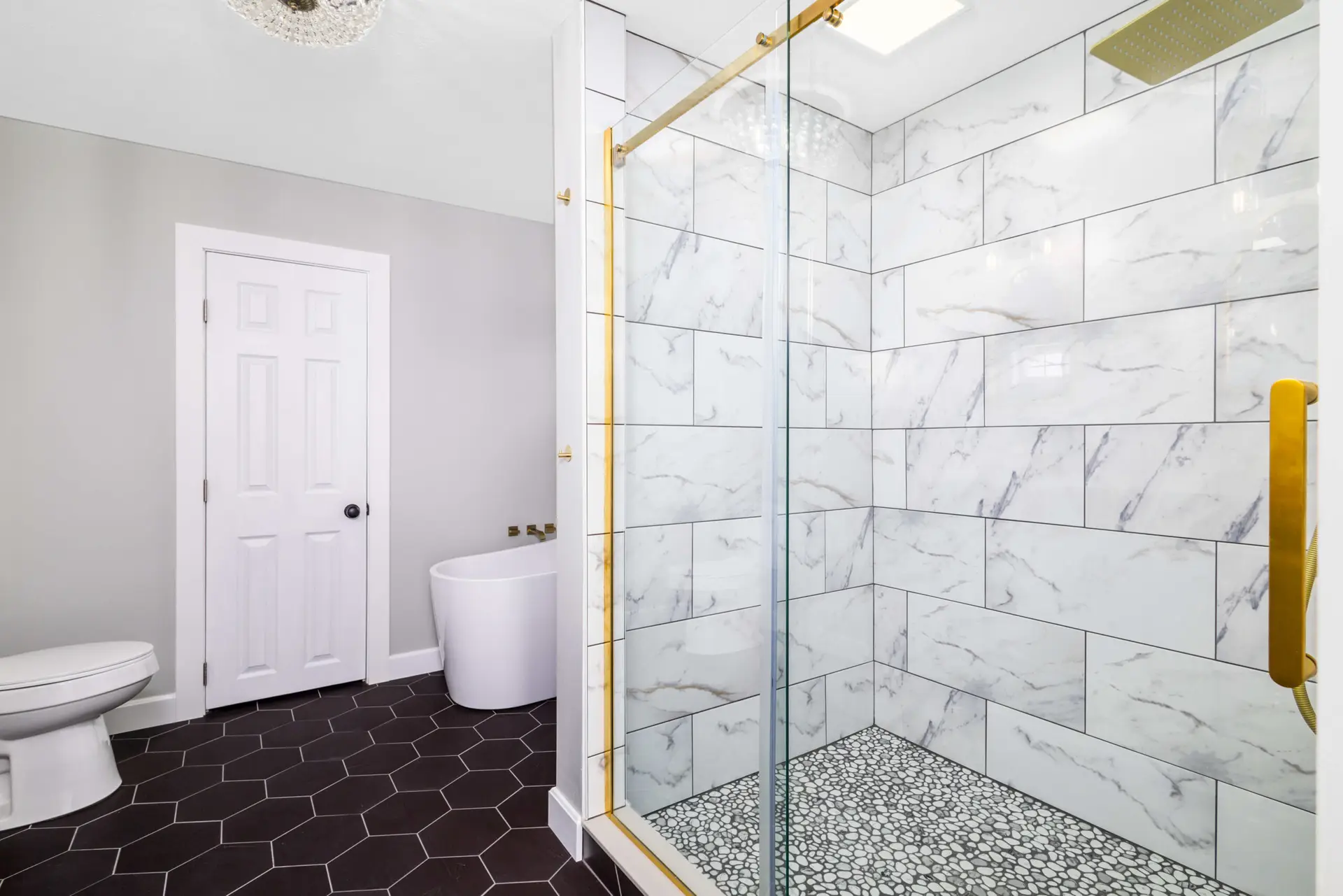 Marble tile shower with brushed gold fixtures and pebble floor by Steel Valley